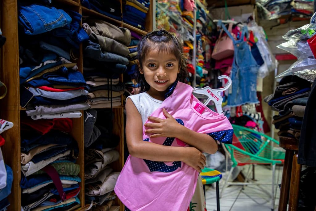 A girl stands holding a pink shirt on a hanger